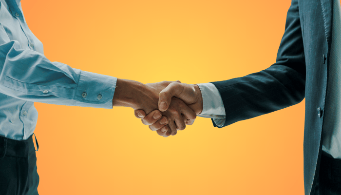 Due persone si stringono la mano, simbolo di accordo e collaborazione su sfondo arancione.