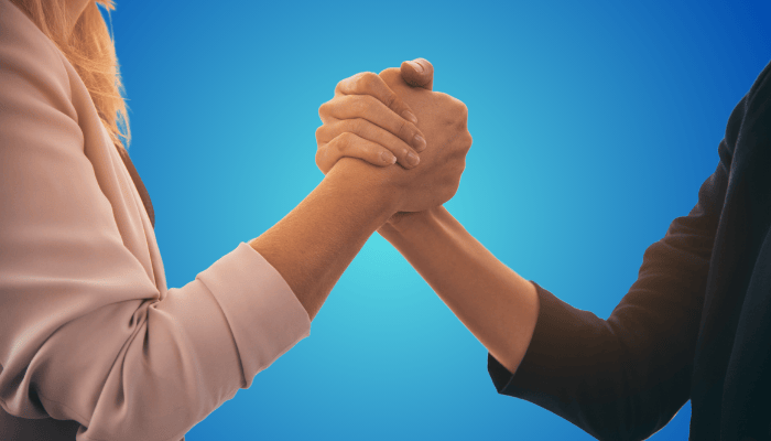 Stretta di mano tra due persone su sfondo blu, simbolo di partnership e collaborazione.